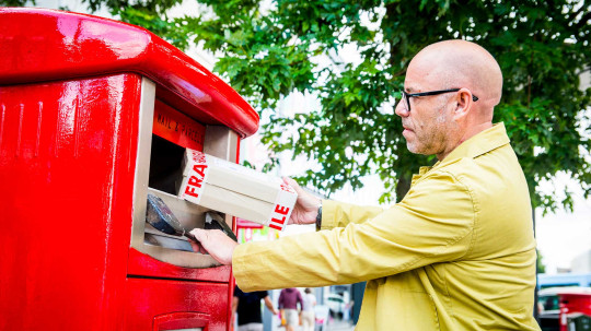 Man posting a parcel in a Royal Mail Parcel Post Box